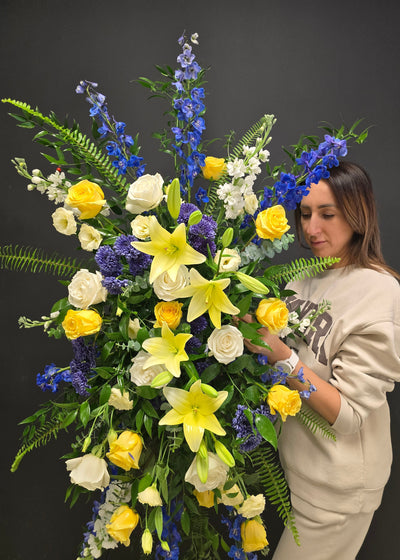 florist is arranging a large sympathy standing spray of fresh flowers on a dark background